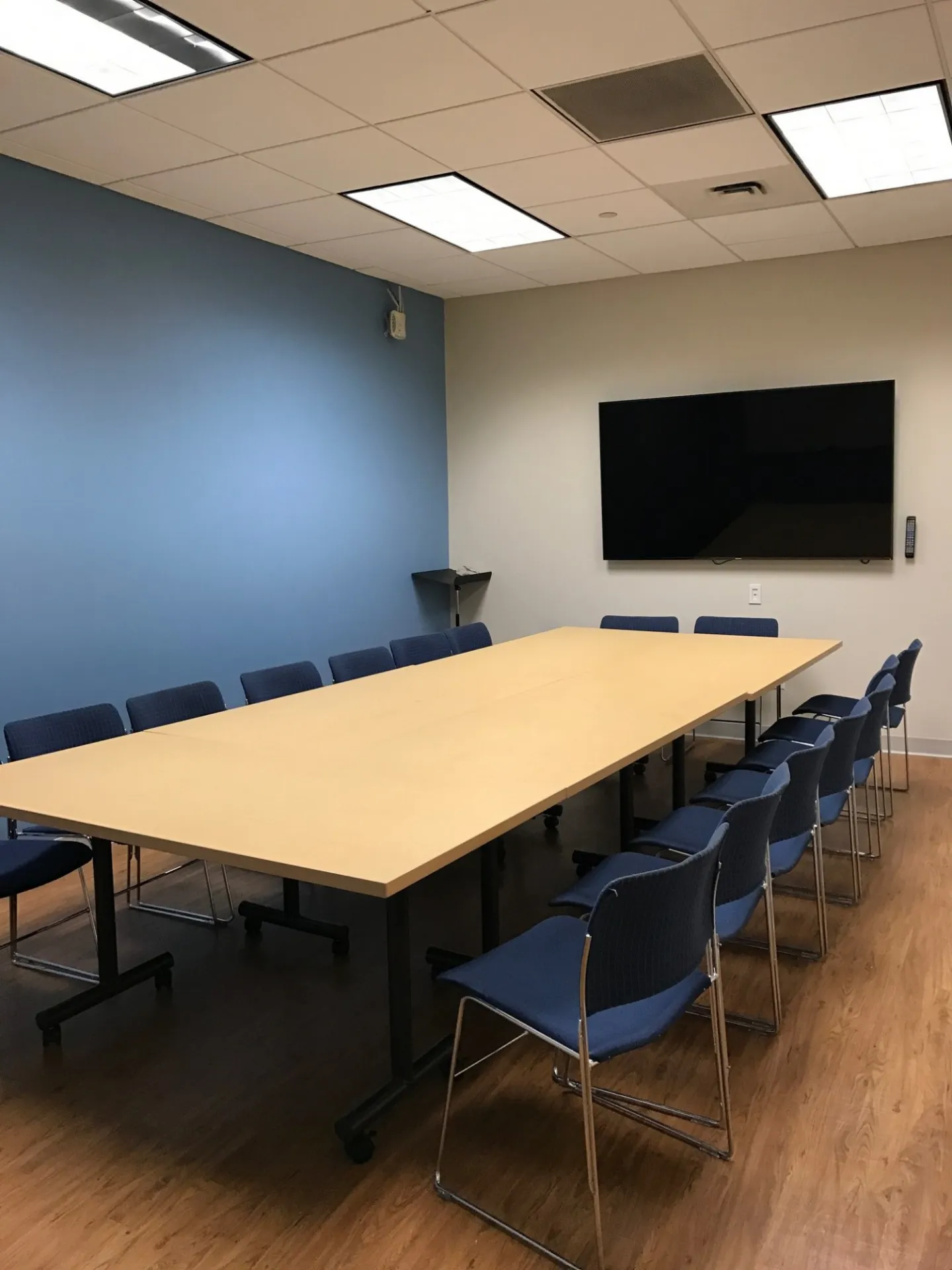 Classroom with long table and moveable chairs and monitor. 